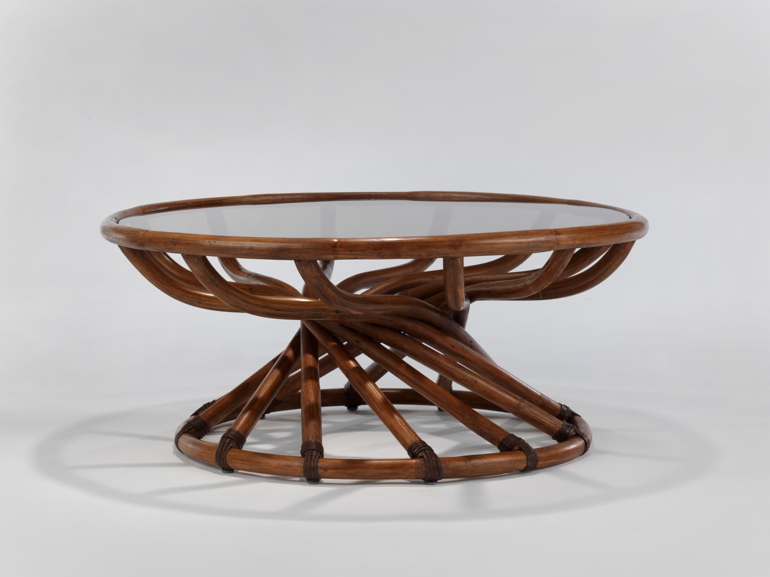 Smoked Glass top low table with curving stained woven bamboo structure in front of white background