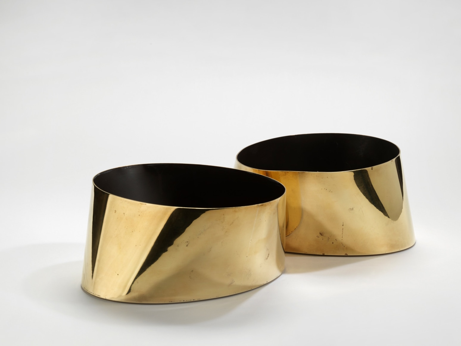 photograph of two circular gold vases with black interiors in a blank room