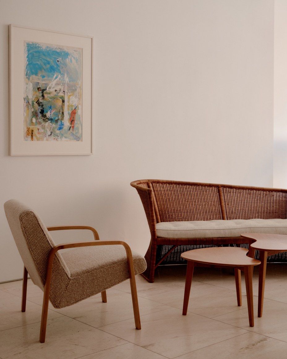 Upholstered armchair by Joseph-Andr&eacute; Motte, rattan loveseat by Louis Sognot, set of low wooden tables by Pierre Guariche and watercolor and gouache work by Eug&egrave;ne Leroy on wall behind.
