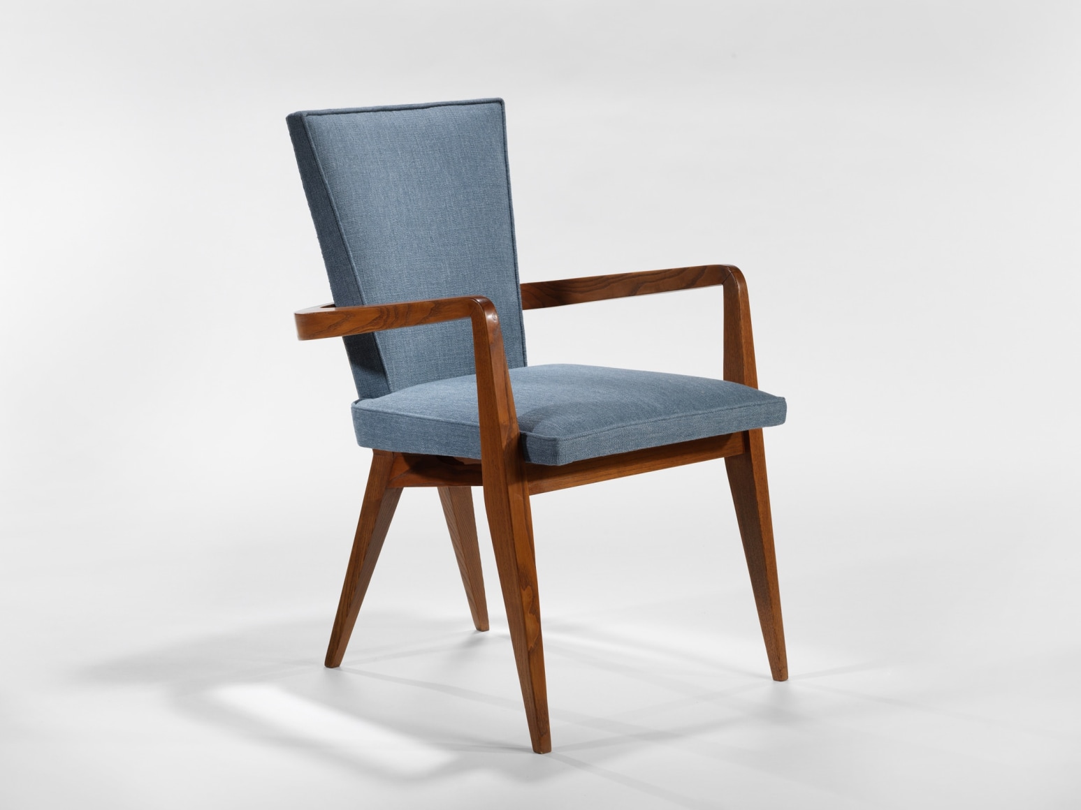 photograph of chair in a blank room with wooden legs and blue upholstery