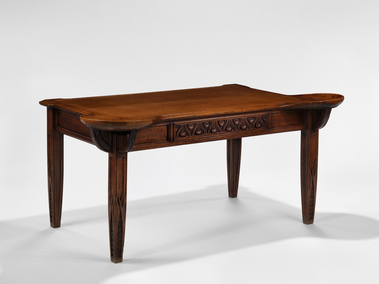photograph in blank room of desk by Gauthier made in wood with detailing throughout, four legs and drawers.