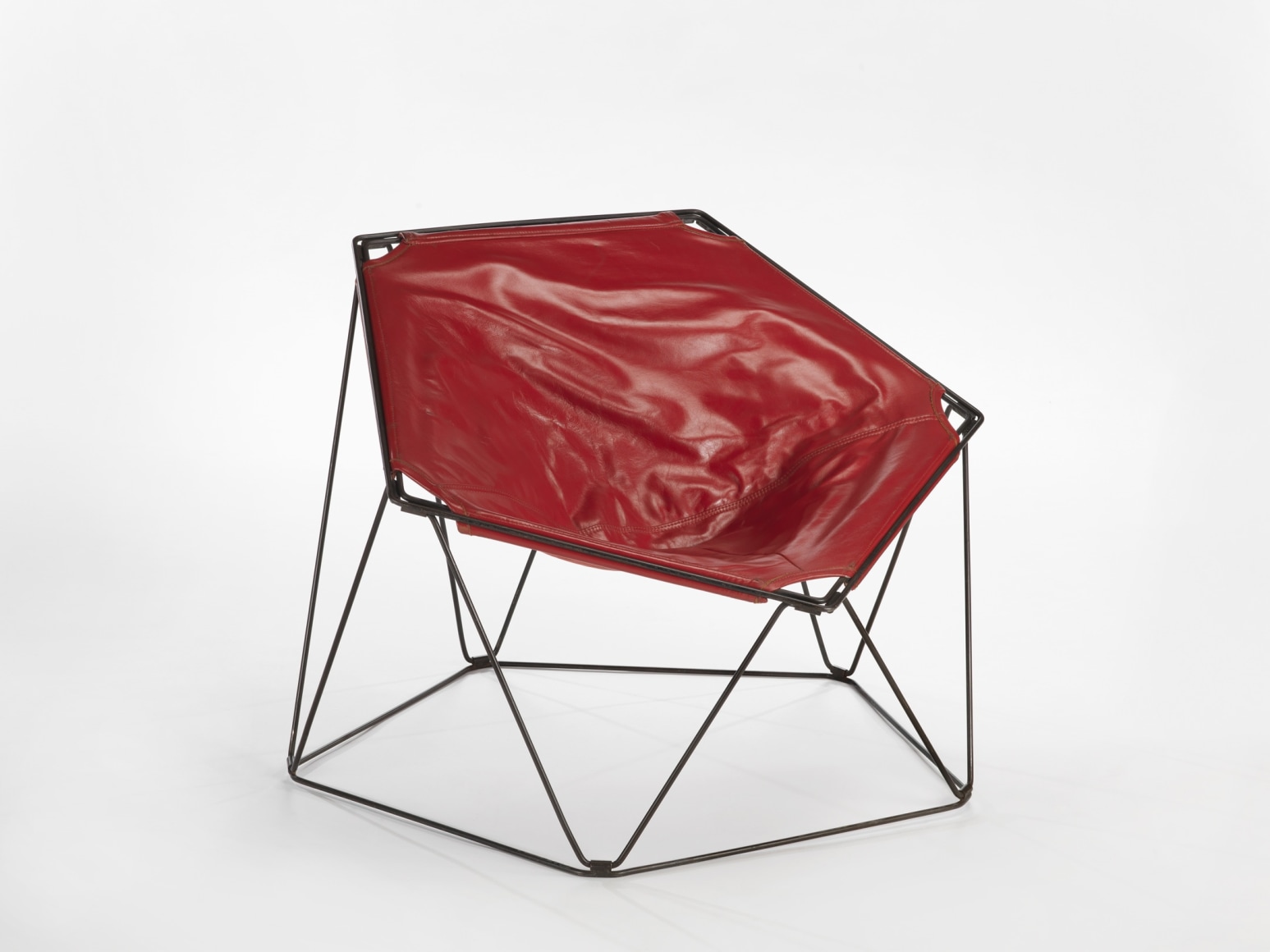 photograph in a blank room of pentagonal shaped chair by Barray with red leather upholstery and black metal wire legs
