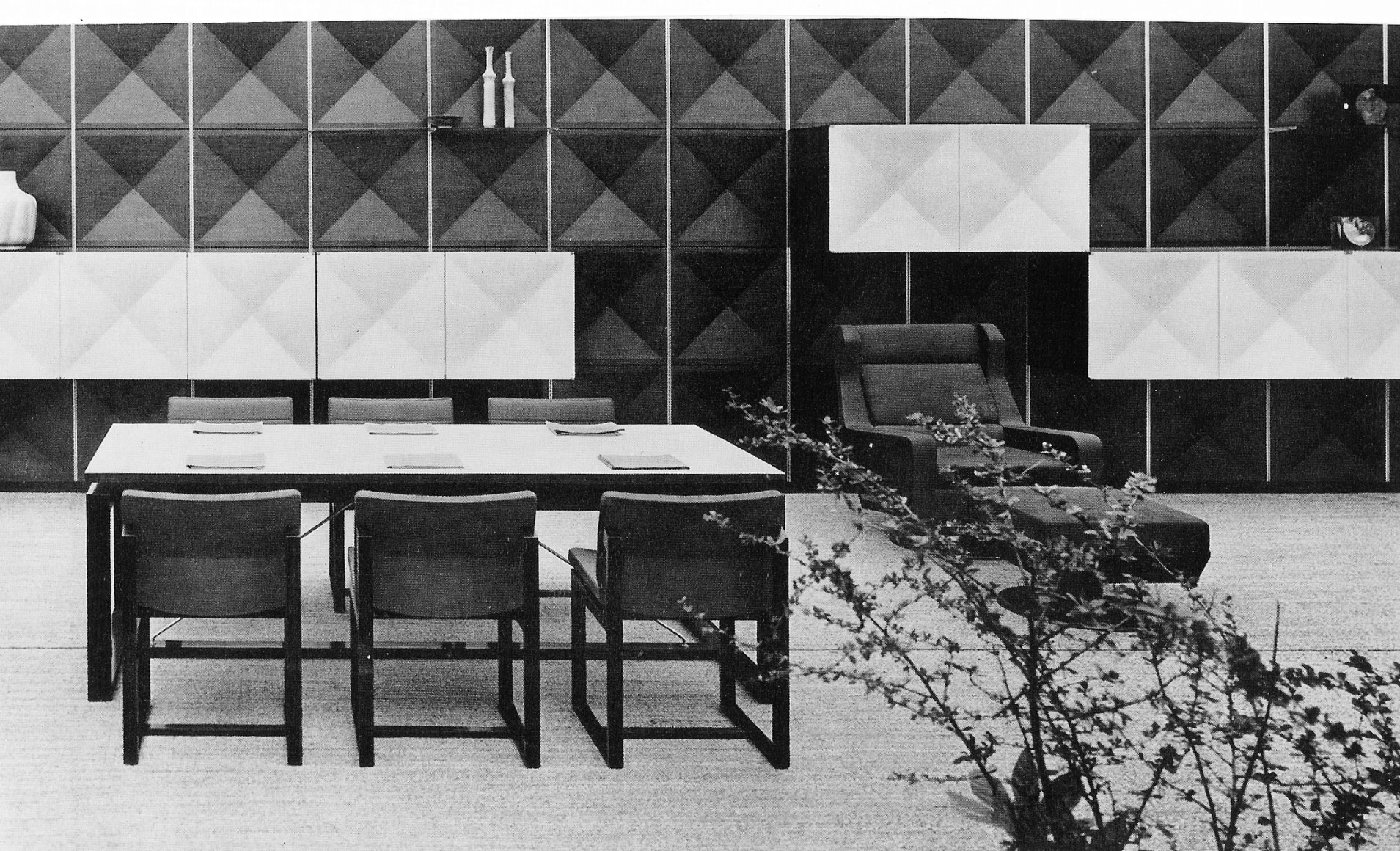 Archival image of a booth set up consisting of a lounge chair with an ottoman, dining table, and matching chairs.