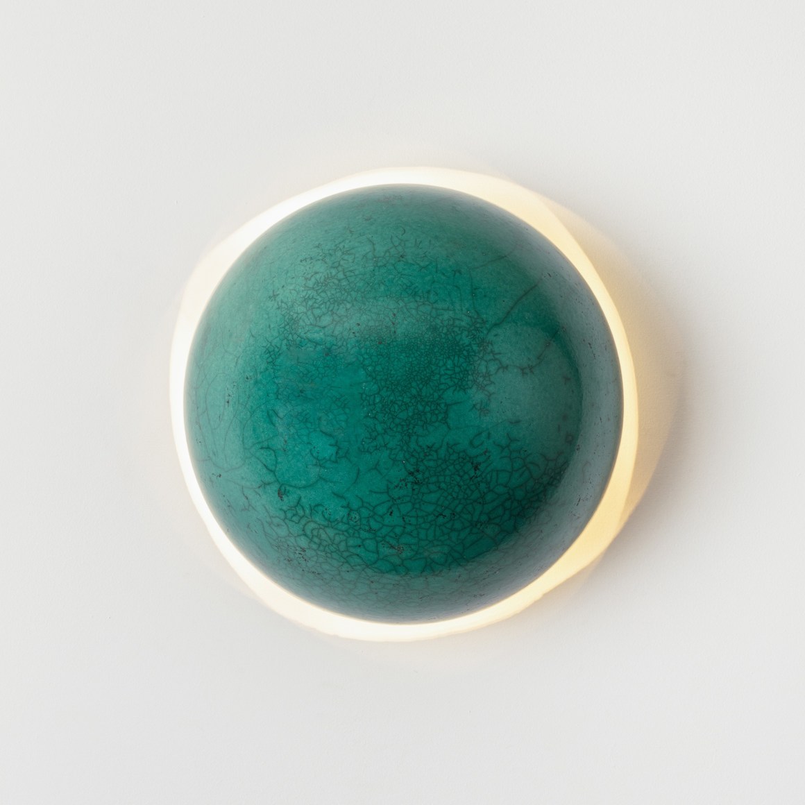 Round green raku glaze wall sconce, light turned on in image.