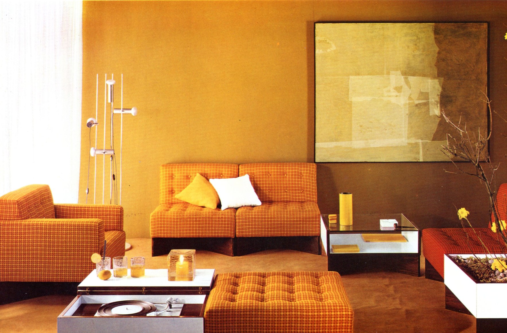 Archival photo of an orange living room with low white and wood tables next to orange plaid love seat, chairs, and ottoman