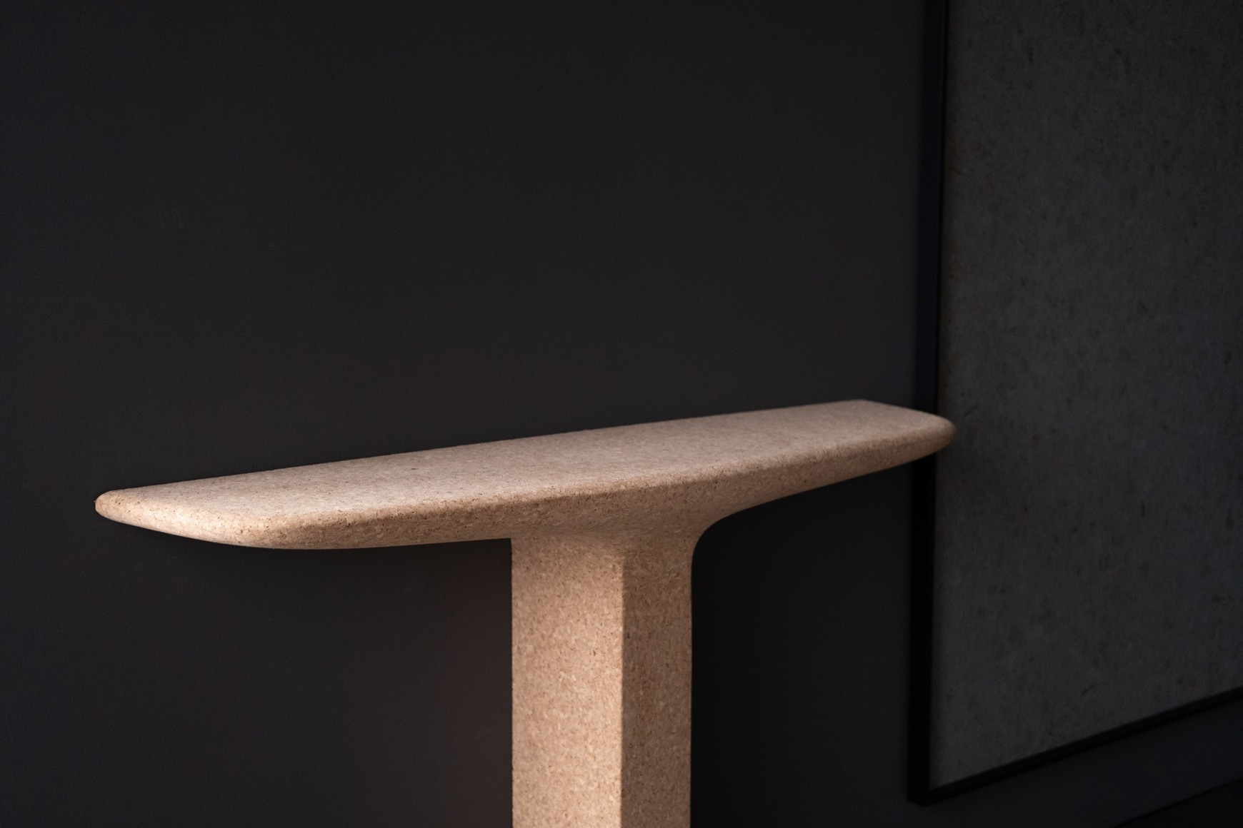 Cork console table with one leg by Noe Duchafour-Lawrance. Photographed against a dark grey wall.
