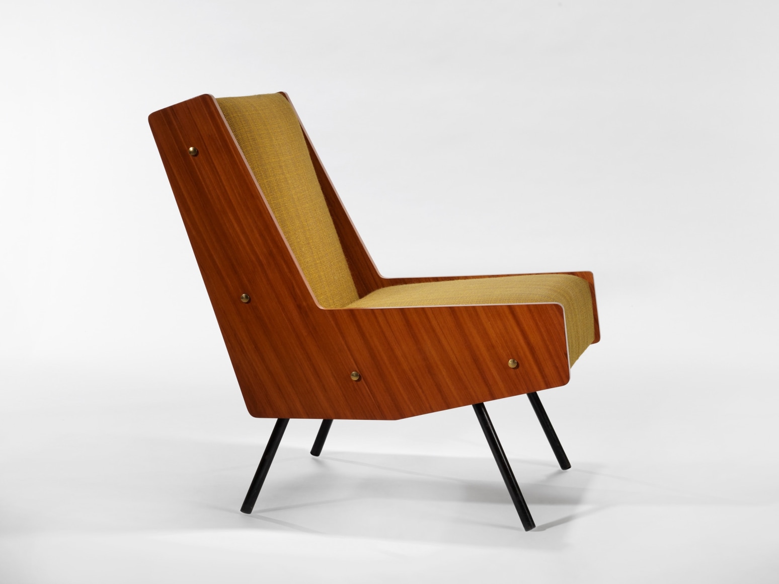 photograph of chair by Motte in a blank room, chair is made of painted metal, mahogany, and fabric