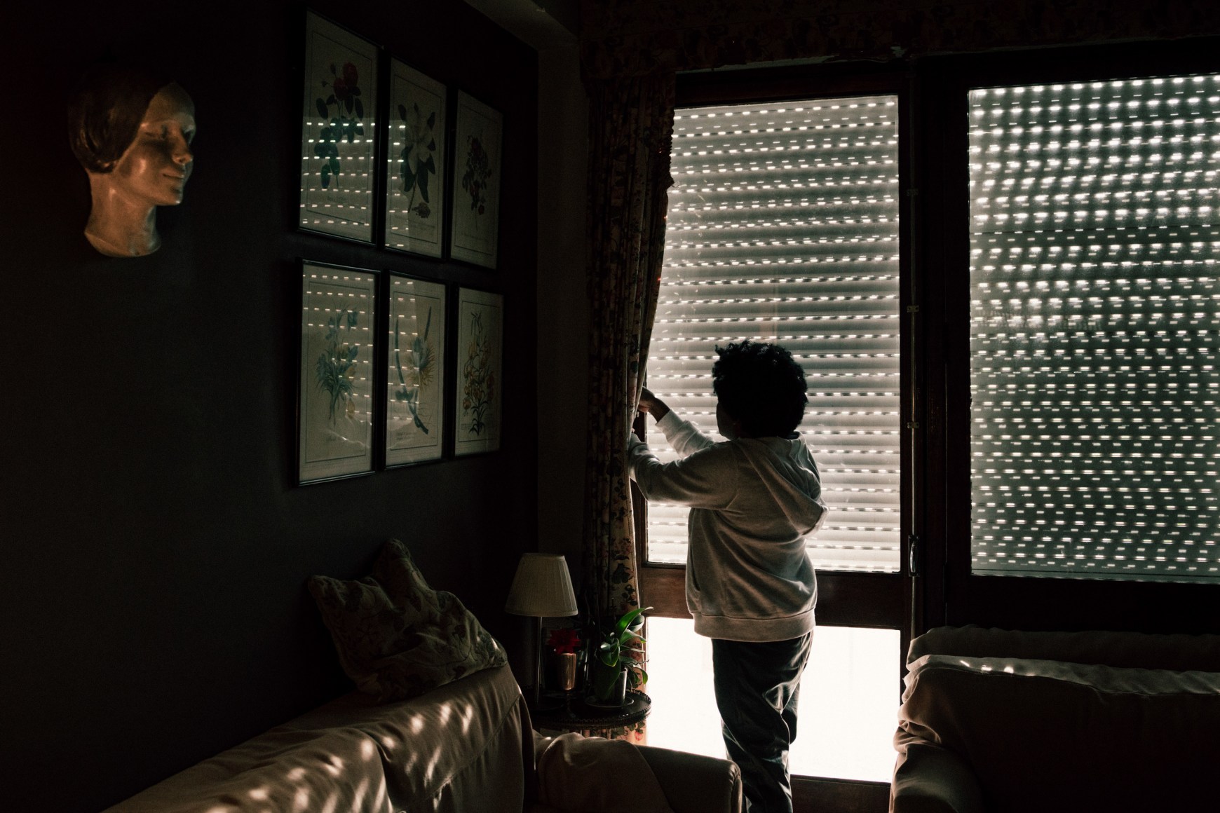 Ana Maria Jeremias opening the window in the home of an elderly lady she cares for in the Estrela neighborhood. Lisbon, Portugal, 2024