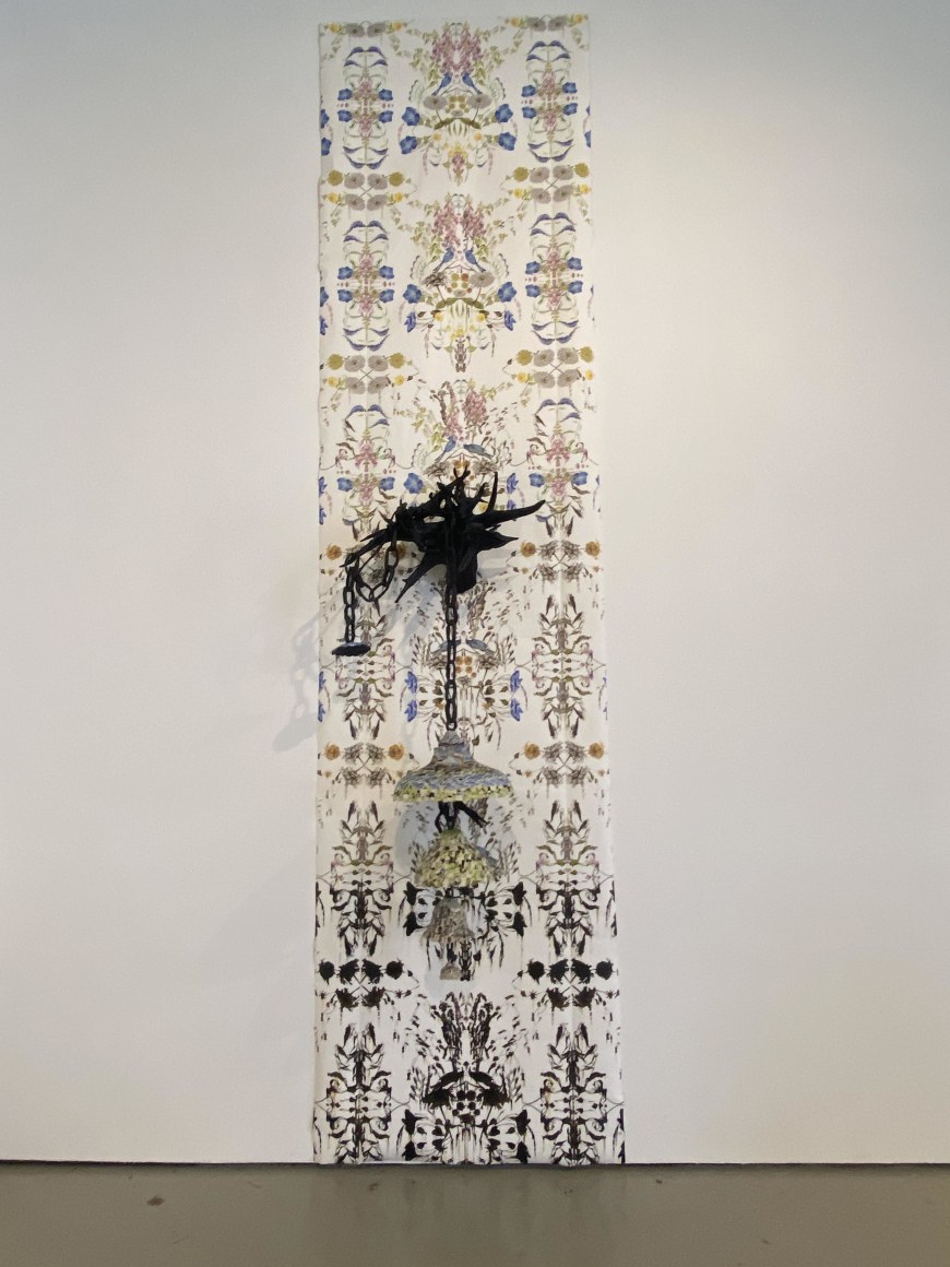 Tall vertical piece made of flora and fauna wall paper with a black cast paper tree root in the center, a four tiered floral lantern hangs from the root.