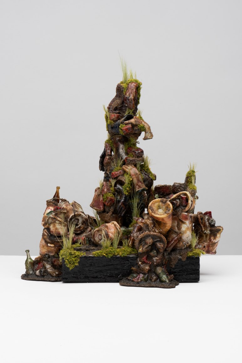 glass sculpture of piles of trash (bottles, buckets etc) with organic matter growing in various places