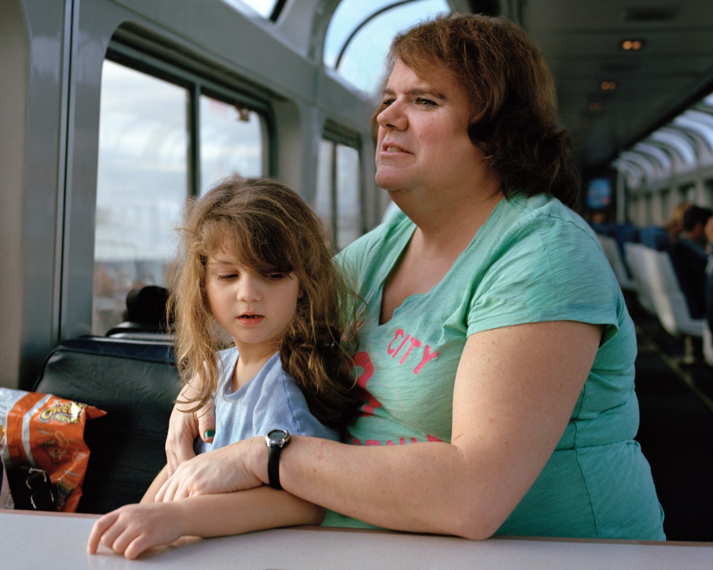 Person with child on lap on a train, by McNair Evans