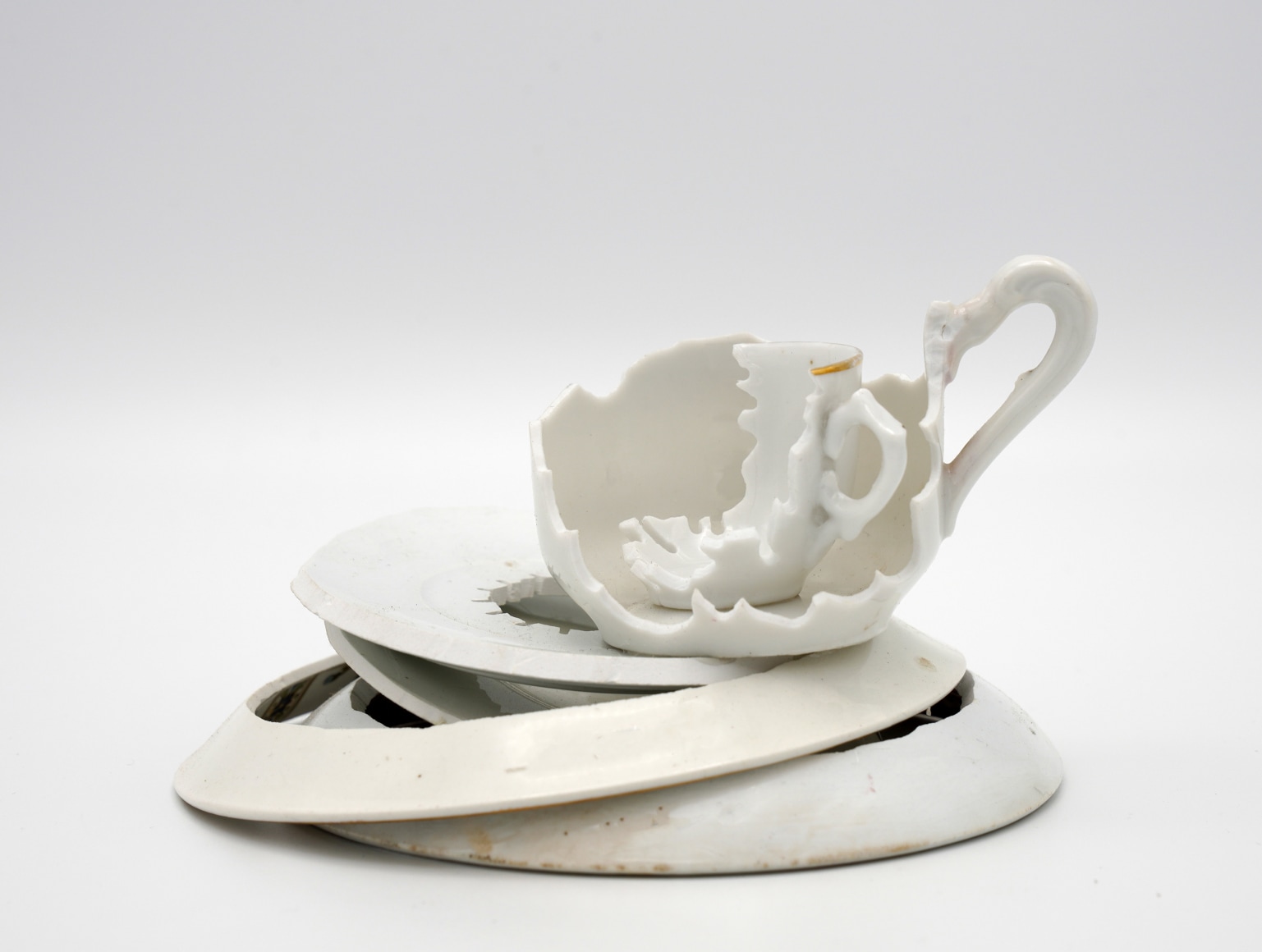 two deconstructed hand cut tea cups sit on a stack of cut porcelain plates