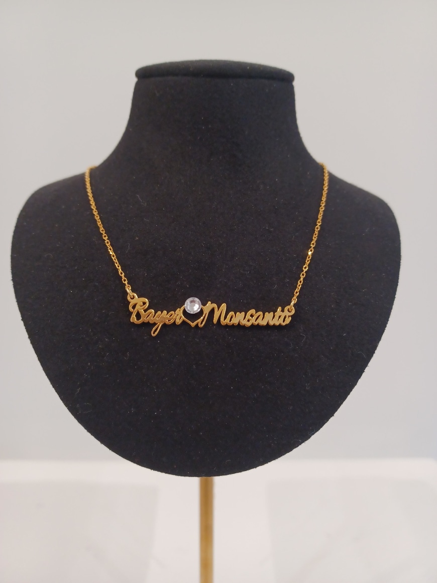 Gold necklace with gem and the text &quot;Bayer Loves Monsanto&quot; on black velvet stand