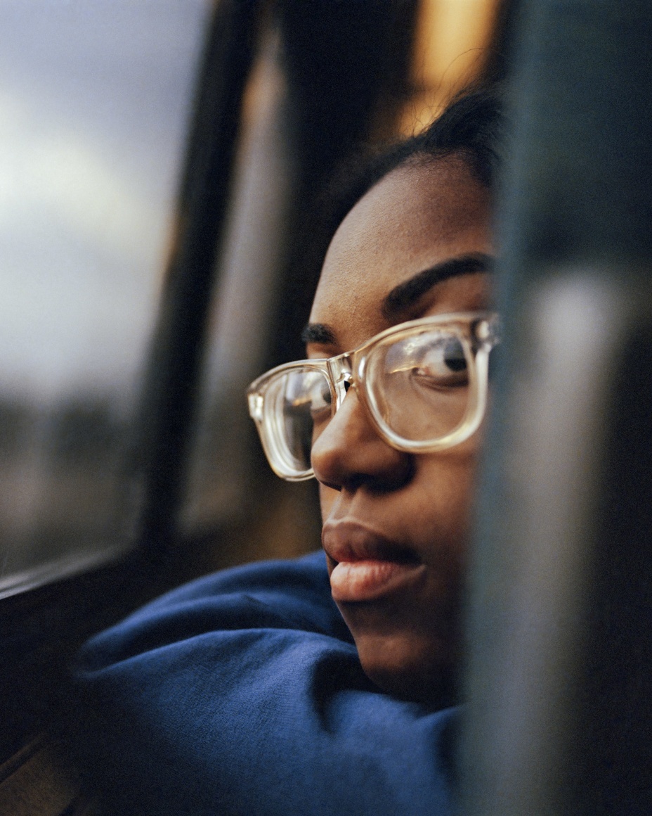 Person with glasses peering back, in train seat