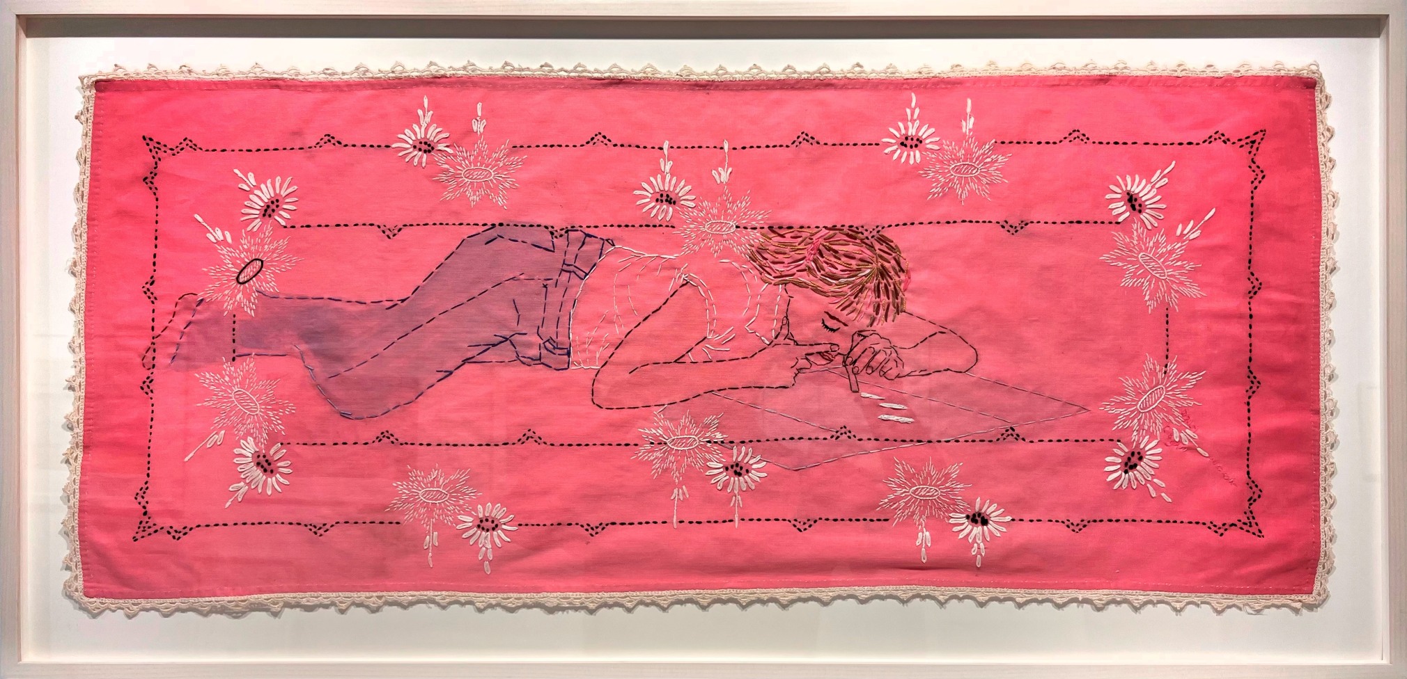 Embroiderd and painted image of a woman laying on her stomach using cocaine. The background is dark ink with a floral border