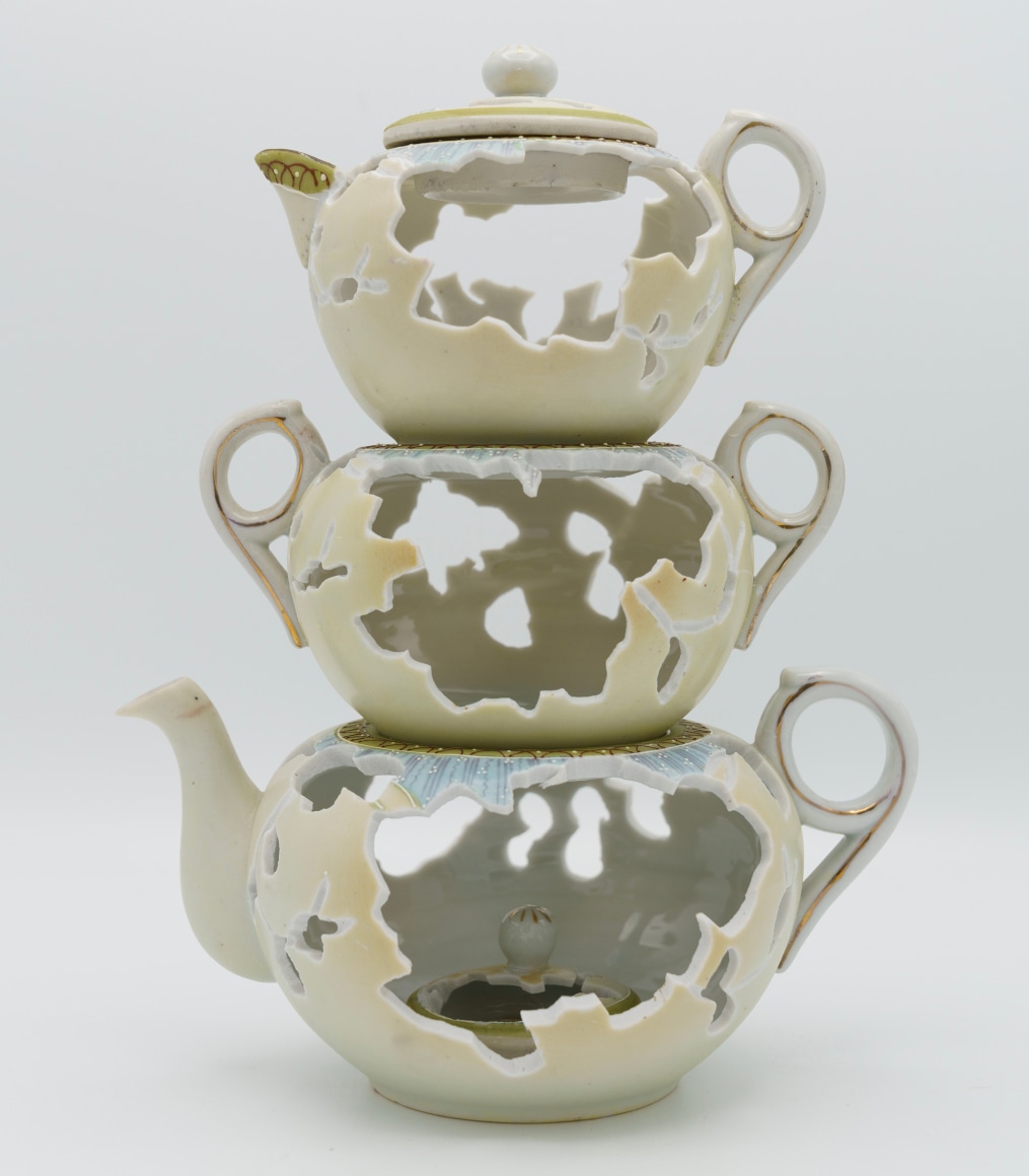 A stack of three tea pots set one on top of the other, the largest on the bottom to the smallest on top. A hand cut holes are in each pot