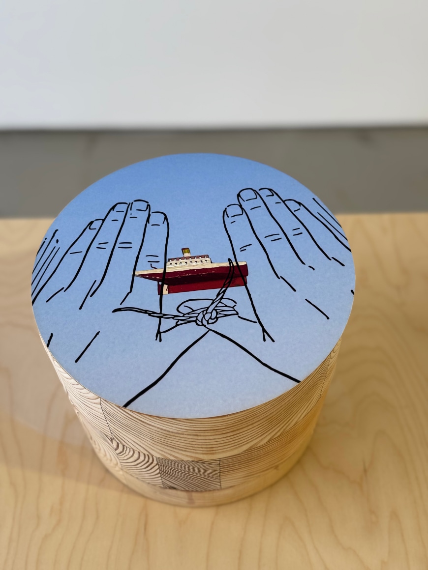 round table top sculpture with mounted archival pigment print of a boat and tied hands. with wooden table as pedestal