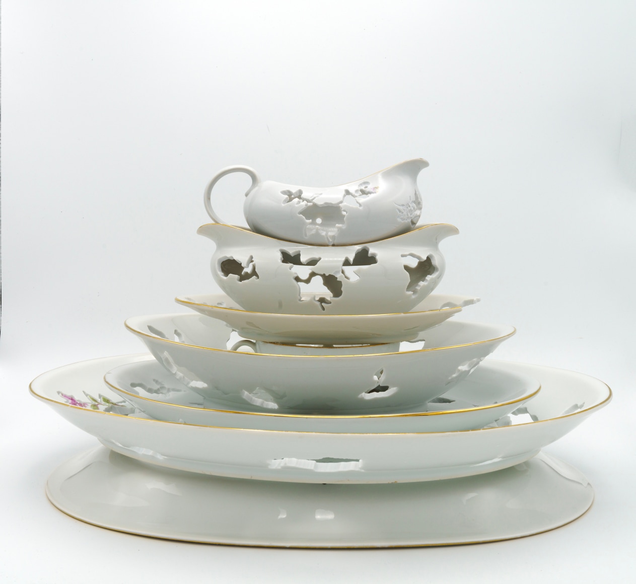 A service set of porcelain china is stacked one on top of the other with a hand cut pattern on each piece