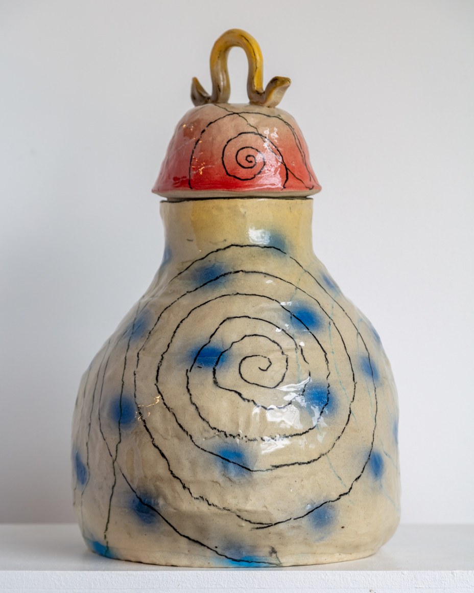 gourd shaped hand coiled vessel with lid. Underglaze has blue dots, black spirals. the lid is red with a yellow handle