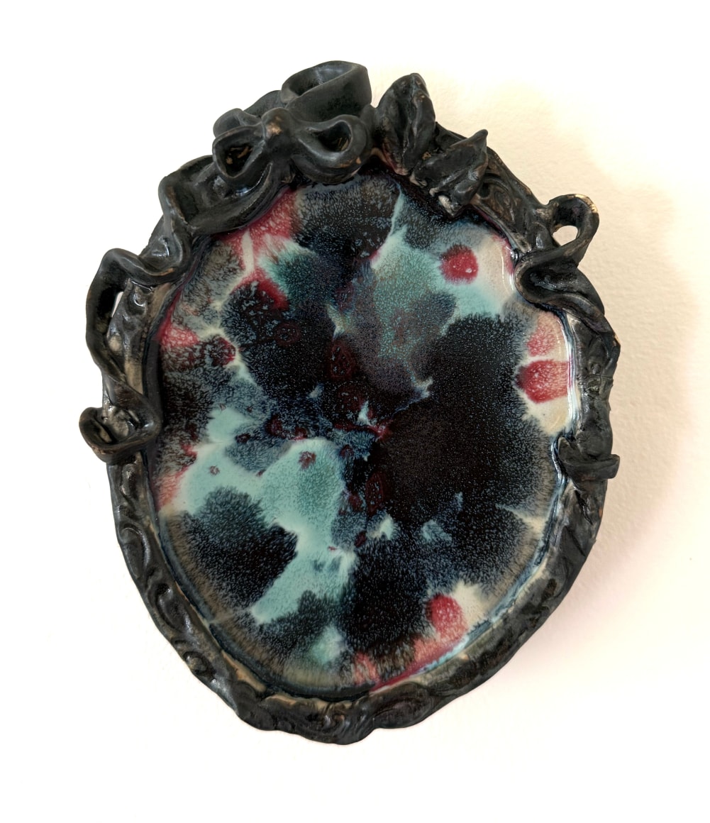 fired and glazed clay object, black and yellow abstract pattern in the center, the edges are ornamental