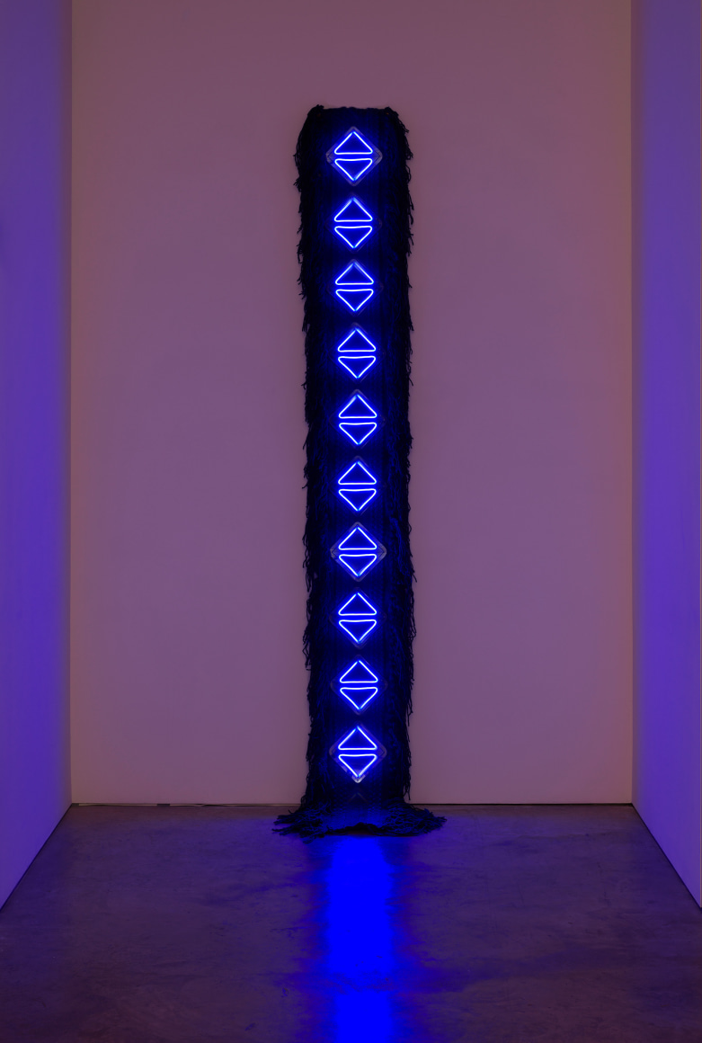 Sandra Monterroso, Como los tri&aacute;ngulos: el agua celeste y la indig&oacute;fera nos devuelven la luz. [Like the triangles: the celestial water and the indigofera give us back the light], 2022. Wool rug dyed with cochineal, cotton cloth dyed with indigo, acrylic, neon, 112 5/8 x 15 3/4 x 1 3/4 in. (286 x 40 x 4.5 cm.)