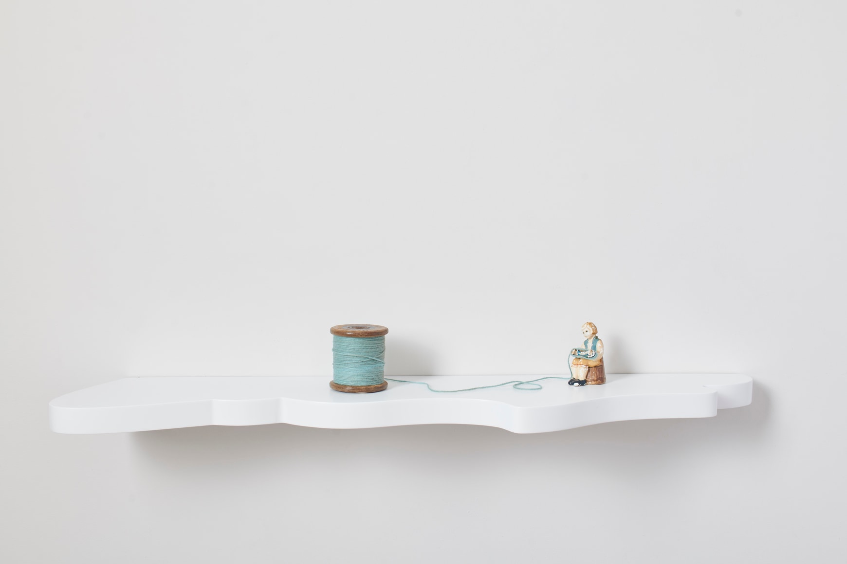 Liliana Porter, Girl With Green Yarn, 2023. Figure on shaped wooden shelf with yarn, 5 &frac34; x 43 &frac12; x 9 &frac12; in. (14.6 x 110.5 x 24.1 cm.)