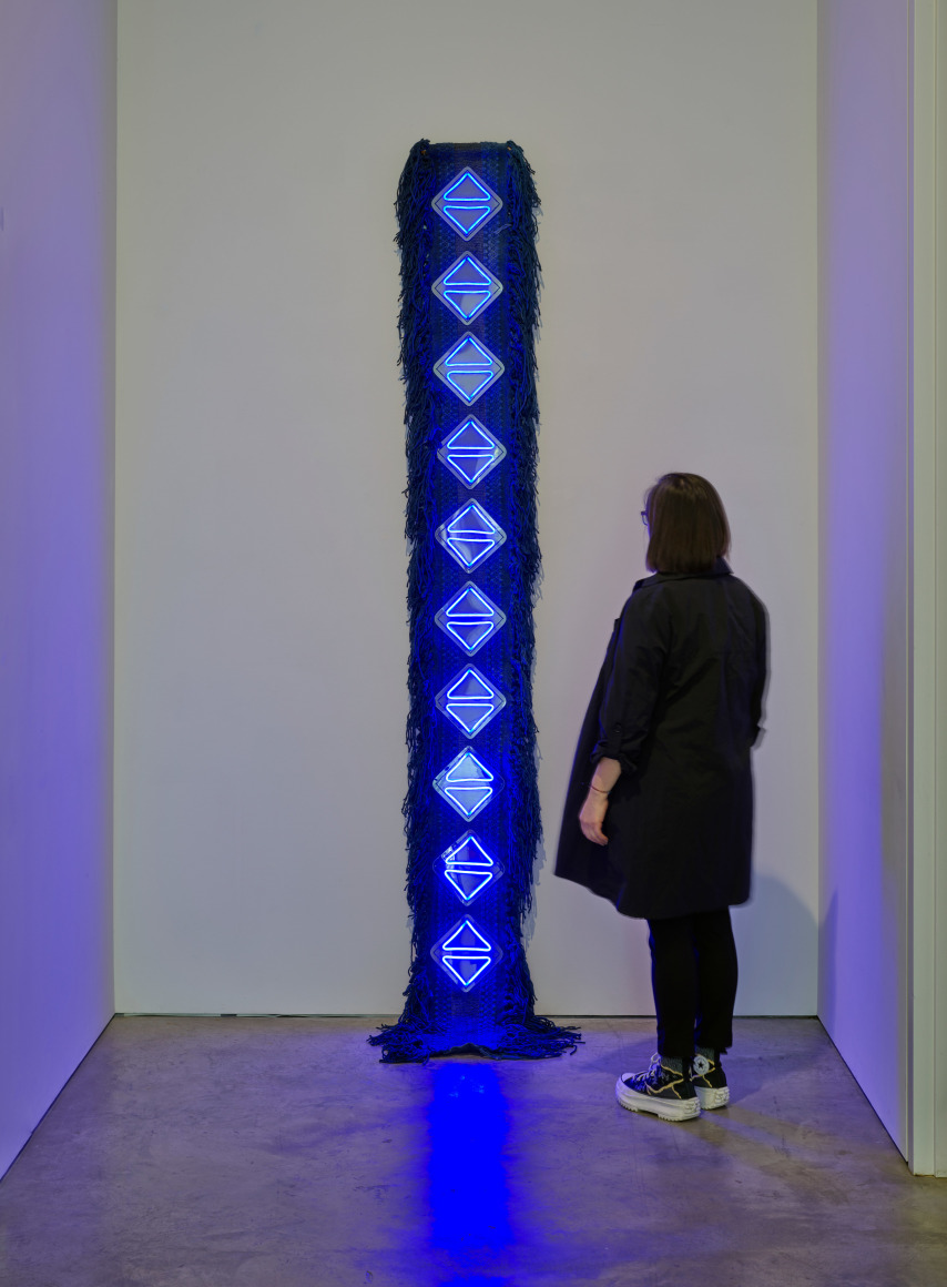 Sandra Monterroso, Como los tri&aacute;ngulos: el agua celeste y la indig&oacute;fera nos devuelven la luz. [Like the triangles: the celestial water and the indigofera give us back the light], 2022, Wool rug dyed with cochineal, cotton cloth dyed with indigo, acrylic, and neon, 112 5/8 x 15 3/4 x 1 3/4 in.