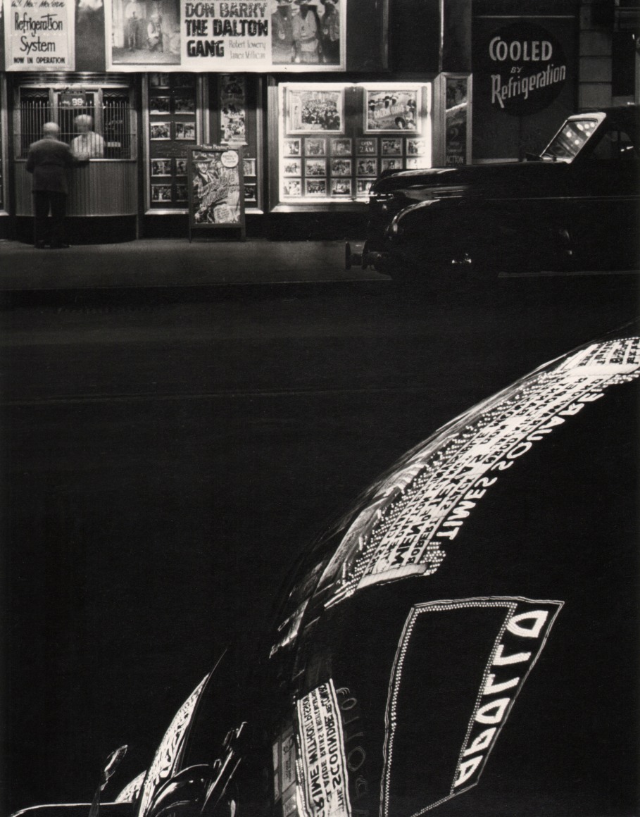 39. Benn Mitchell, Times Square 42nd Street, New York City, ​c. 1955. Lit signs reflecting on a car hood at night.