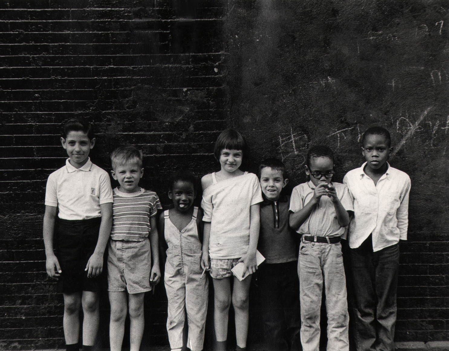 26. Beuford Smith, 7 Kids, Lower East Side, ​1965. A line of children standing against a dark brick wall.