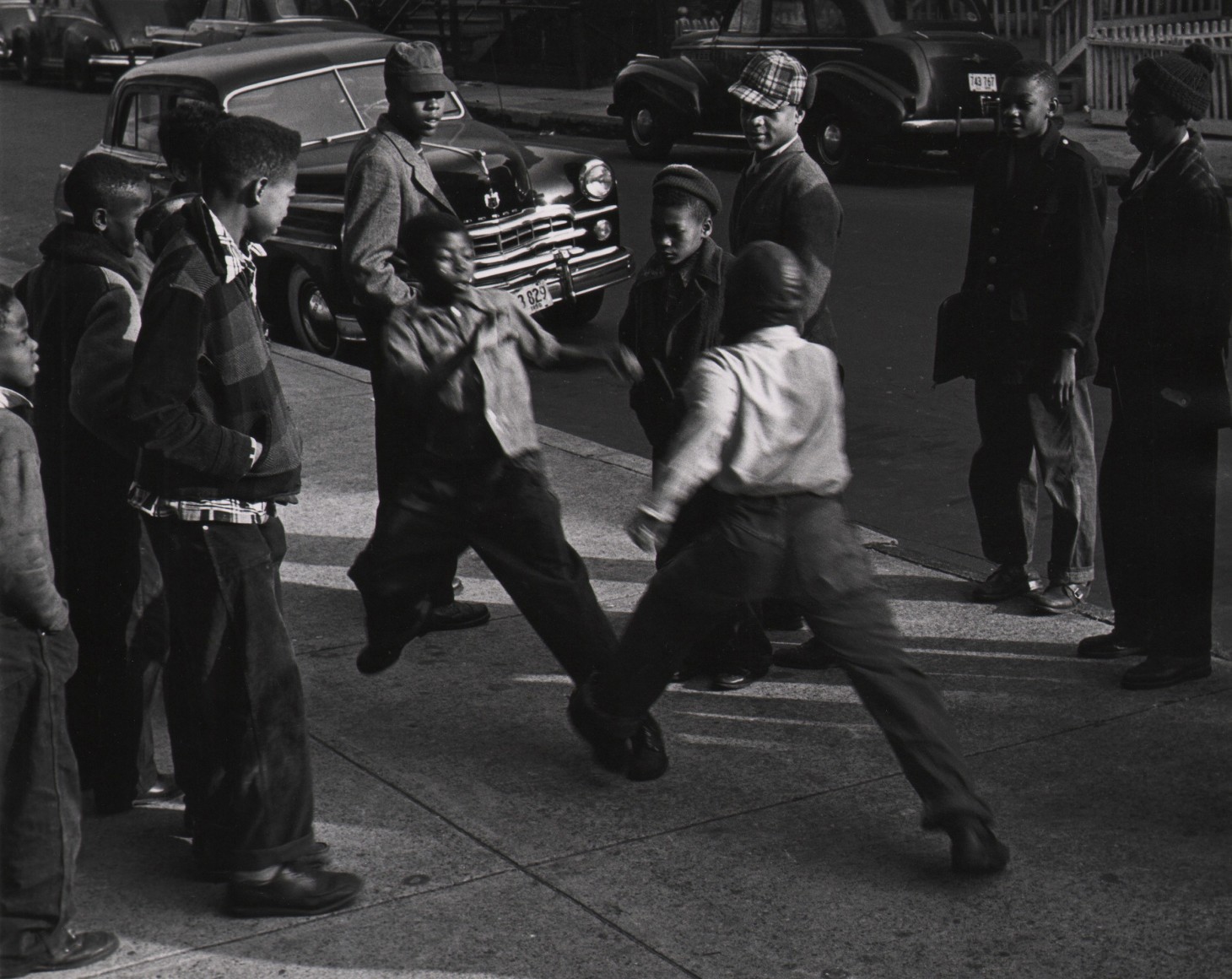 Marvin E. Newman, Chicago, ​1950. A group of boys stand on the sidewalk in a circle around two boys blurred with motion, facing each other.