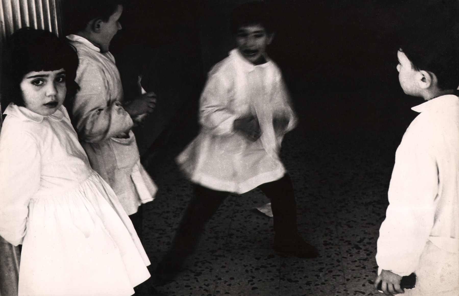 21. Renzo Tortelli, Piccolo Mondo, 1958&ndash;1959. High contrast image. Three children in white around a fourth child in the center, blurred with motion.
