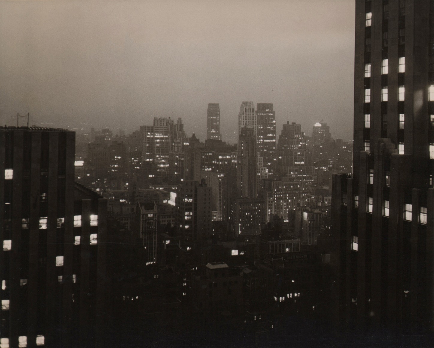 Paul J. Woolf, New York Skyline at Night, ​c. 1935. Night time cityscape. Two close buildings on the left and right foreground with skyscrapers across the background center.