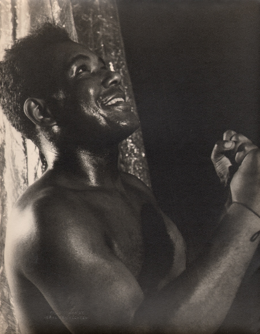 18. Carl Van Vechten, Rex Ingram in Stevedore, 1934. Shirtless figure in semi-profile smiling up and to the right of the frame with fists held up in front of his chest.