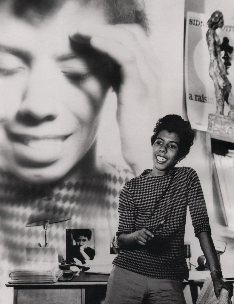 05. David Attie, Lorraine Hansberry at her Bleecker Street apartment, ​1959. Subject poses leaning against a desk with a close-up photograph of herself superimposed on the wall in the background.