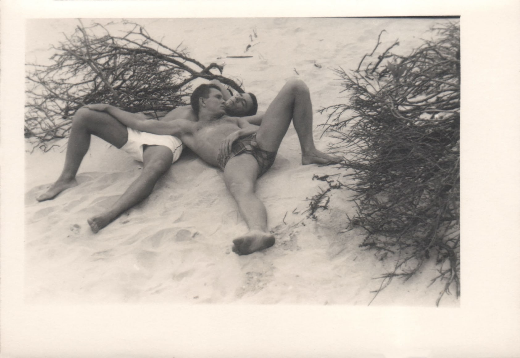 PaJaMa, Ted Starkowski, Chuck Howard, ​c. 1945. Two men in swimsuits lay on the beach, one leaning against the other's chest. Each has one leg bent and one extended.