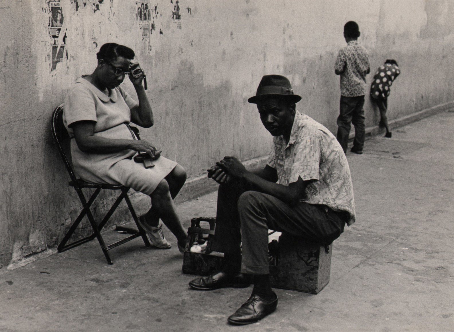 13. Beuford Smith, Untitled, Lower East Side, ​1970. A man and woman sit on a folding chair and box on the sidewalk; two children stand behind them.
