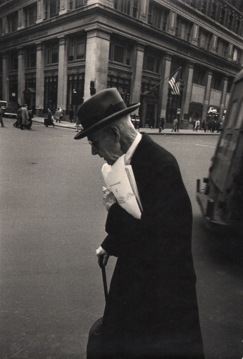 3B. Simpson Kalisher, Untitled, ​c. 1958. An old man in profile holding a cane and papers crossing the street.