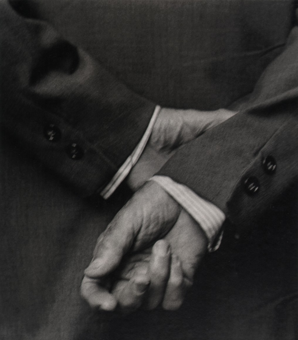 28. Beuford Smith, Two Buttons, ​n.d. Close up of one hand holding the opposite wrist behind a suited man's back.