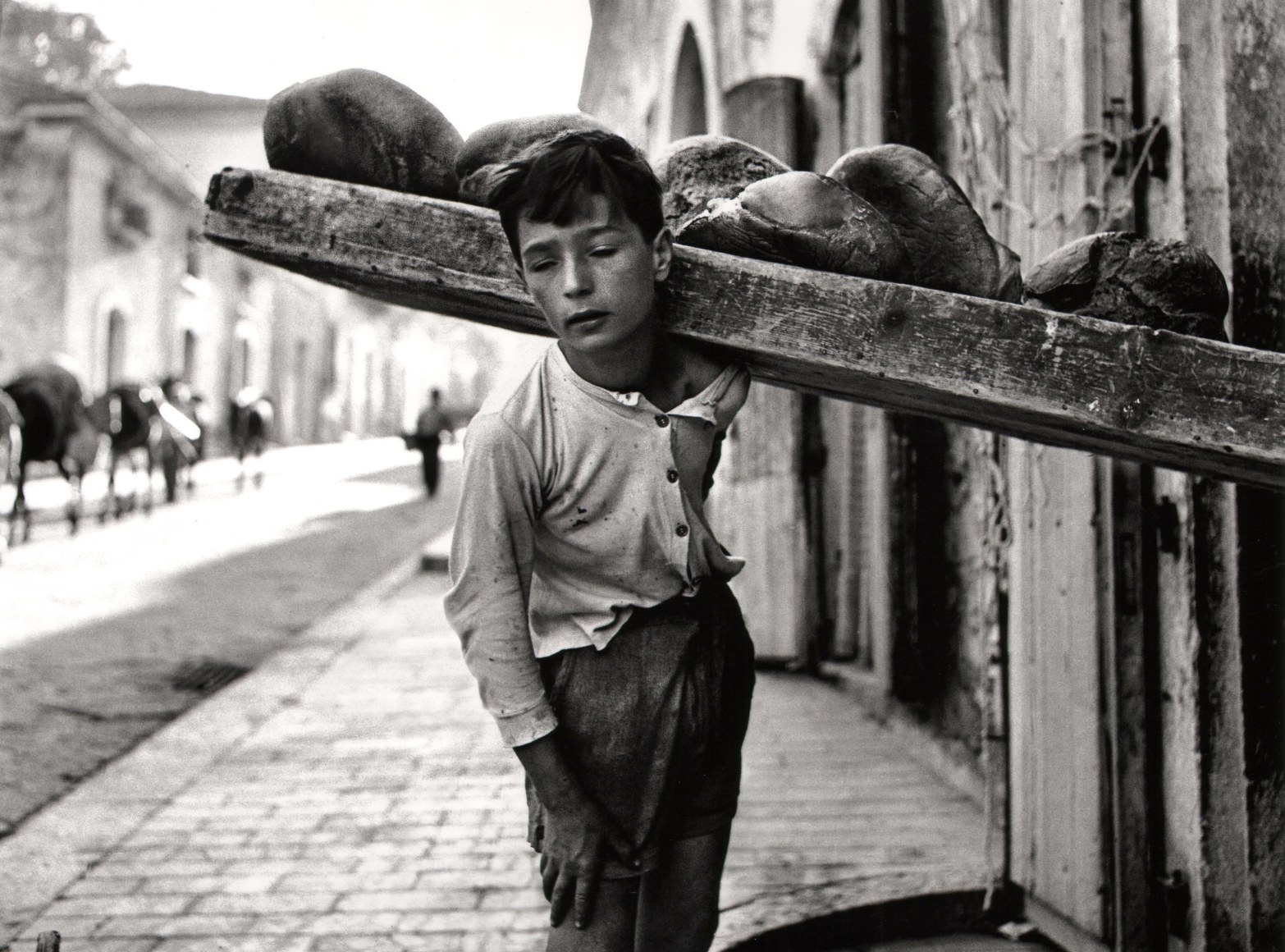 Nino Migliori, Bread Carrier, 1956. A boy carries bread on a wooden plank on his left shoulder.