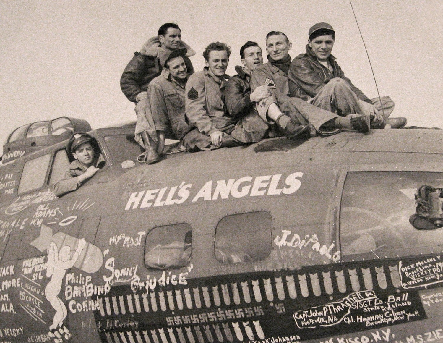 23. Loomis Dean, Untitled, ​c. 1942. Six men sit atop a small aircraft that reads &quot;Hell's Angels&quot;