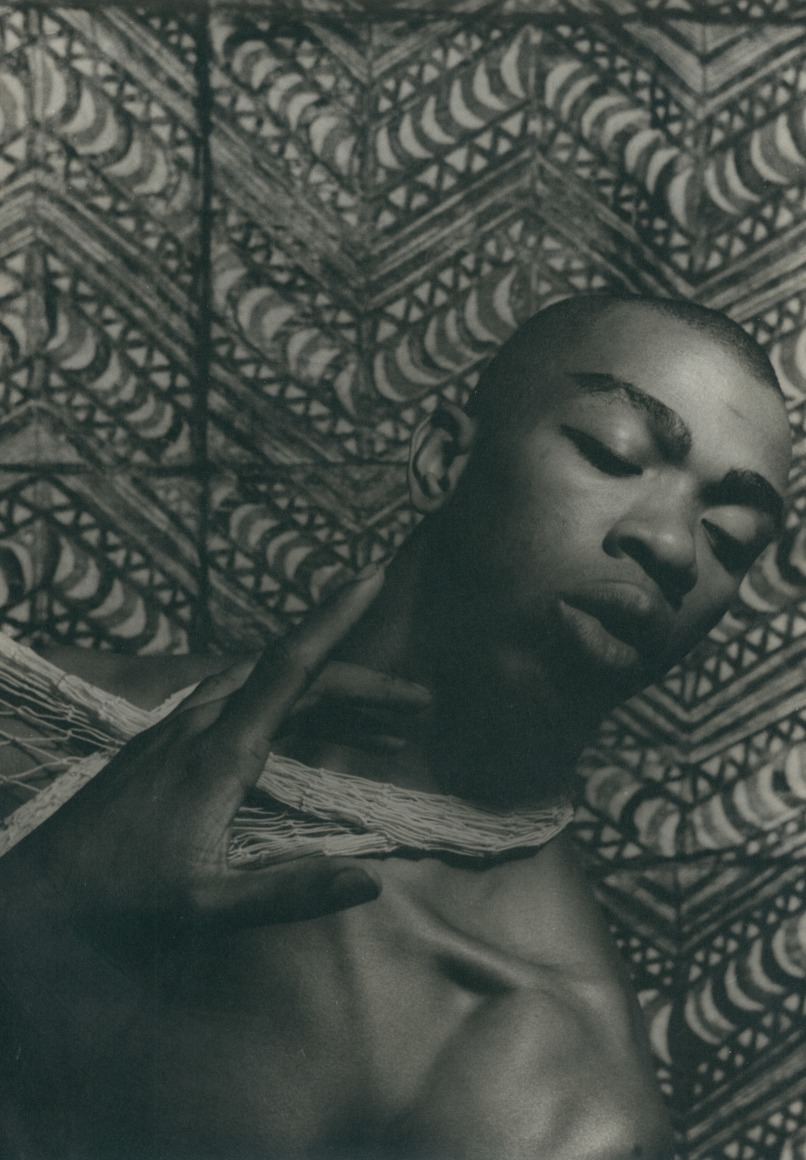 16. Carl Van Vechten, Geoffrey Holder, 1954. Bust length portrait with bare-chested subject at an angle from the lower left to upper right of the frame, eyes cast to the lower right and one hand held up in front of his chest.