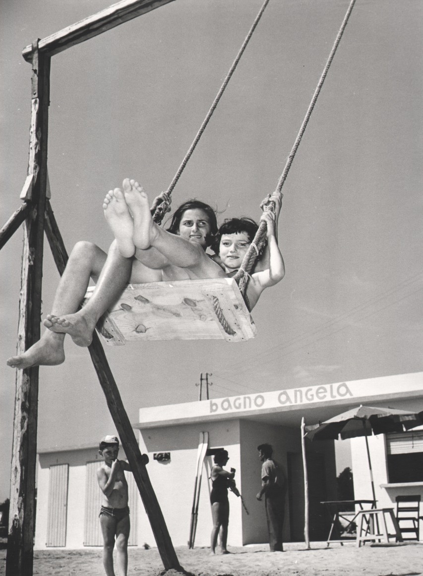 Nino Migliori, Children by the Sea, 1954. Two girls on a swing photographed from a low angle.