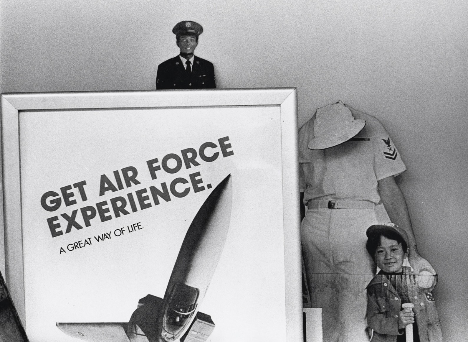 40. Beuford Smith, Get Air Force Experience, Harlem, ​1982. A sign that reads &quot;Get Air Force experience. A great way of life.&quot; in front of cardboard cutouts of men and a young boy.
