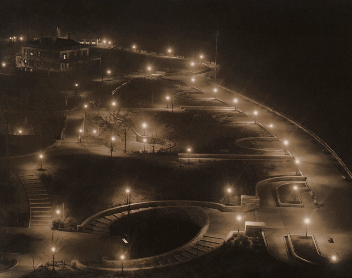 Paul J. Woolf, Carl Schurz Park, ​c. 1935. Night time view of a park with street lights illuminating various walking paths and stairways.