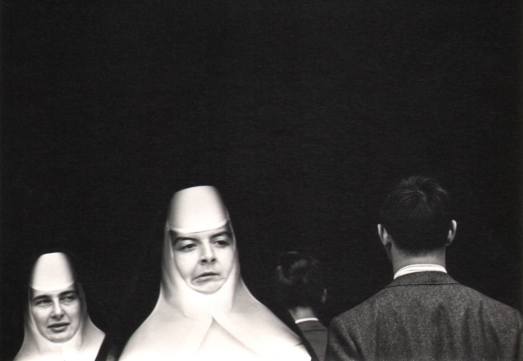 26. Donald Blumberg, In Front of St. Patrick's Cathedral, ​1965. The heads of two nuns, facing the camera, and two men, facing away appear in the lower third of the otherwise black frame.