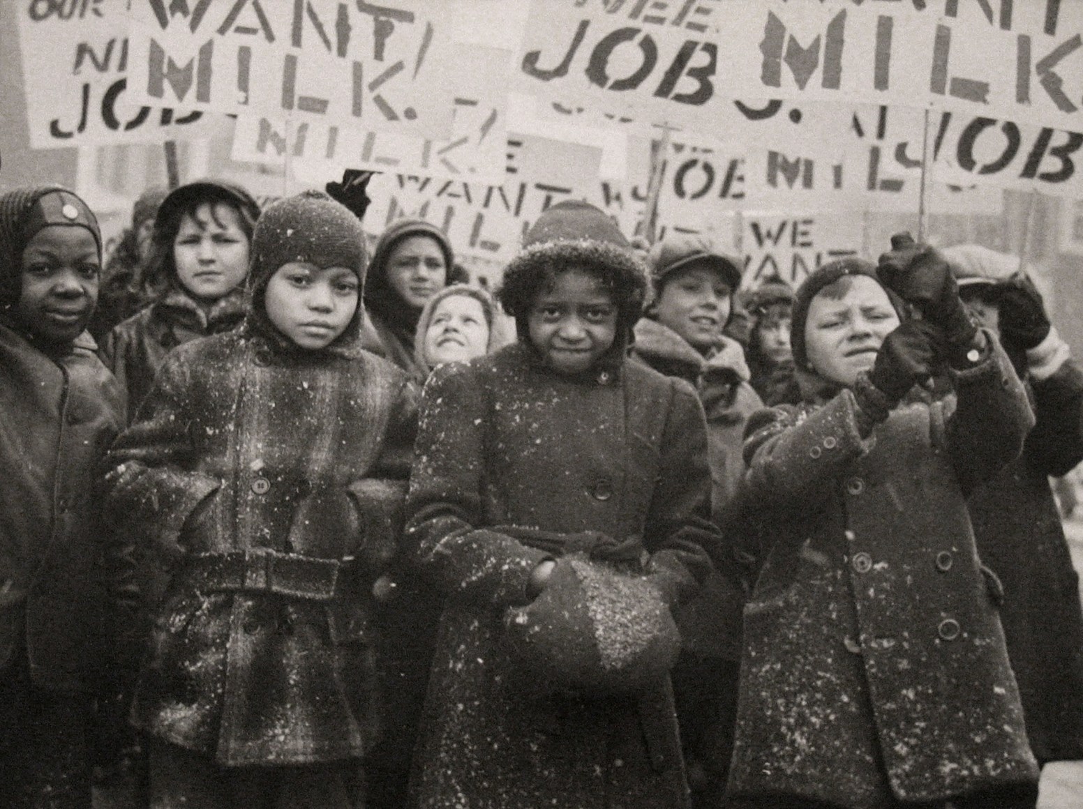 18. Gordon Coster, Untitled, ​c. 1938. Crowd of children in winter coats holding signs above their heads. Signs are in partial view, but the words &quot;MILK&quot; AND &quot;JOB&quot; can be seen.