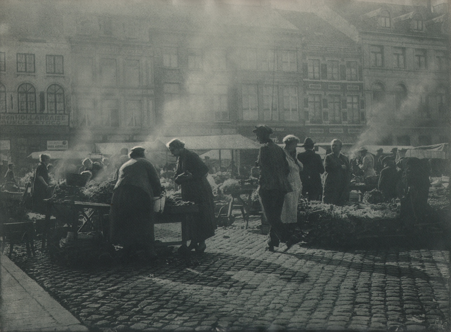06. L&eacute;onard Misonne, Untitled, c. 1937. Many figures on a cobbled market street with steam rising from various booths. Gray/green-toned print.