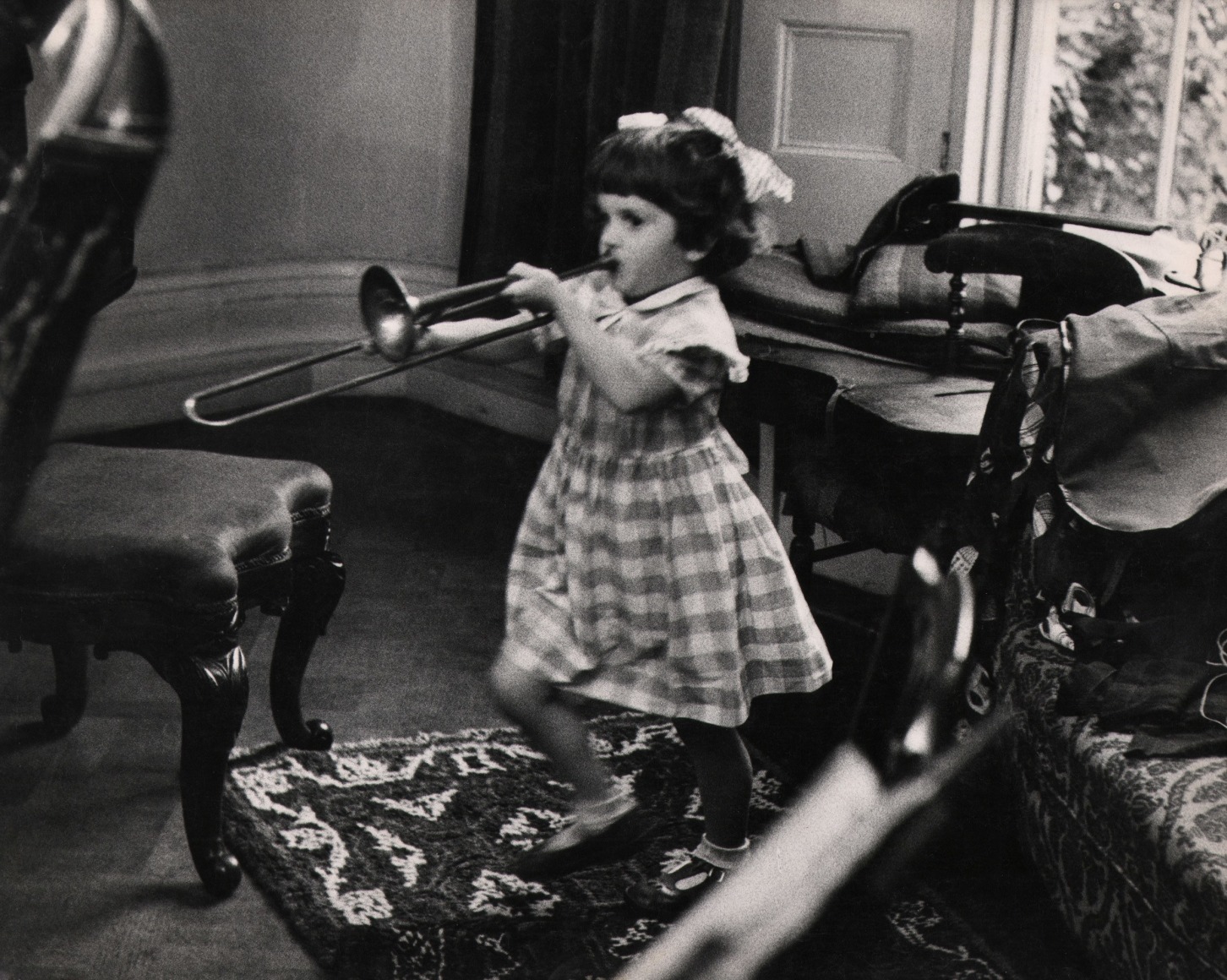 32. Grace Robertson, One of a series...on the four children of Dennis Mathews, c. 1957. A little girl in a checkered dress plays a trombone in a sitting room.