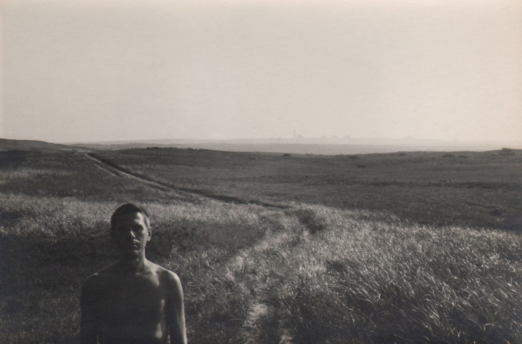 PaJaMa (Jared French), Paul Cadmus, Nantucket, ​1946. Subject stands shirtless in the foreground in the lower left of the frame, a large field in the background.