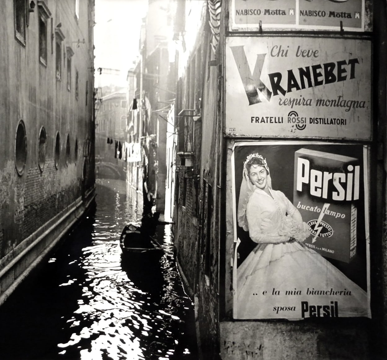 Nino Migliori, Venice, 1958. A canal with one boat running between buildings. Advertisements on the right.